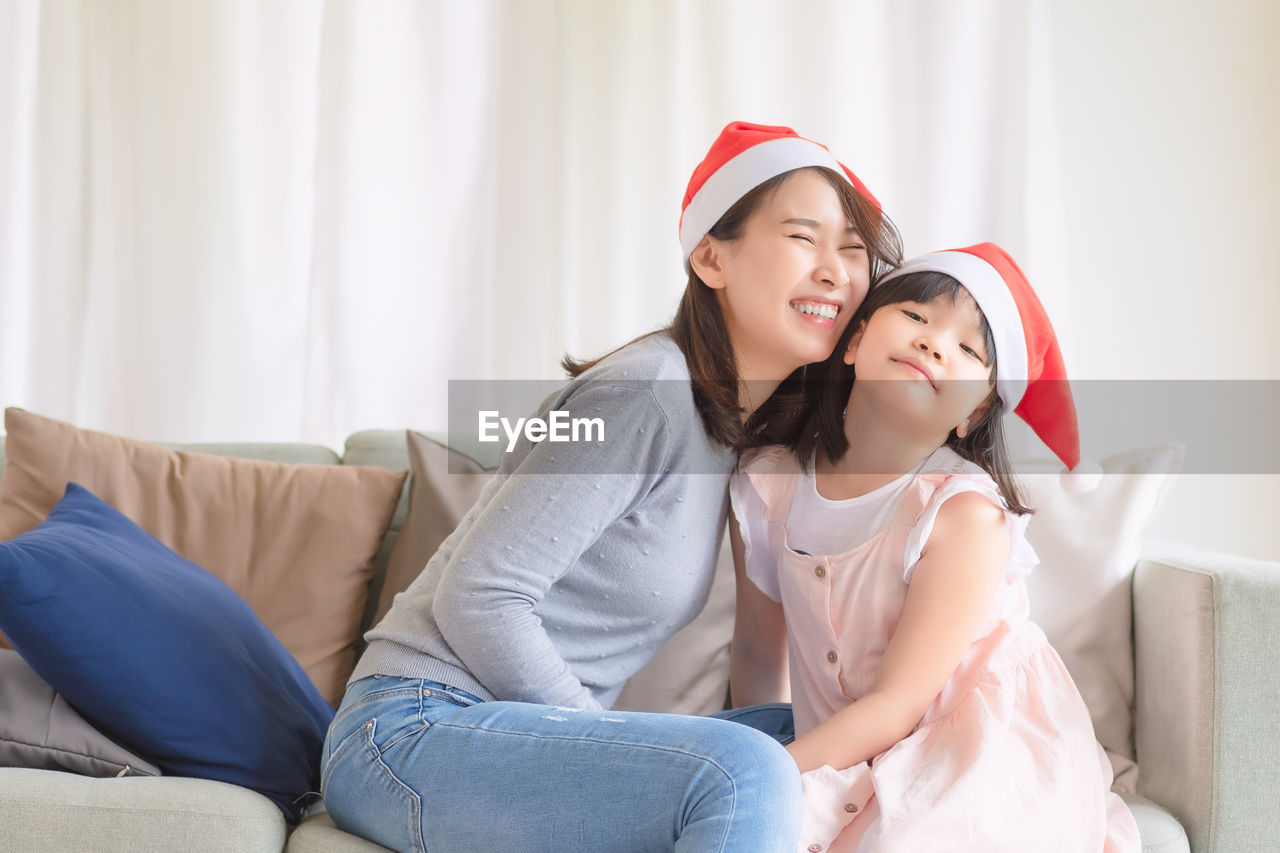 Smiling mother and daughter sitting on sofa at home