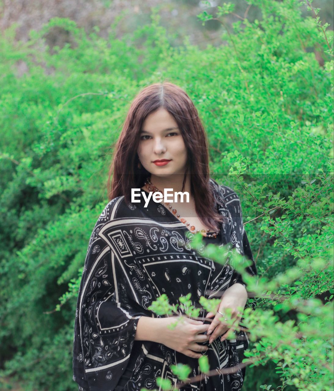 PORTRAIT OF YOUNG WOMAN STANDING AGAINST PLANTS