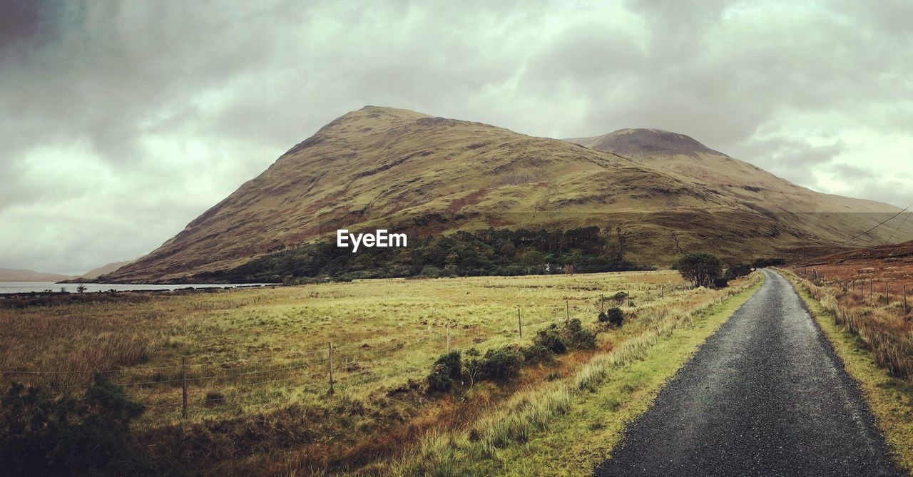 Road leading towards mountains against cloudy sky