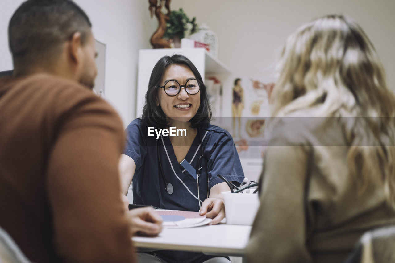 Happy female healthcare expert discussing over chart with couple in medical clinic