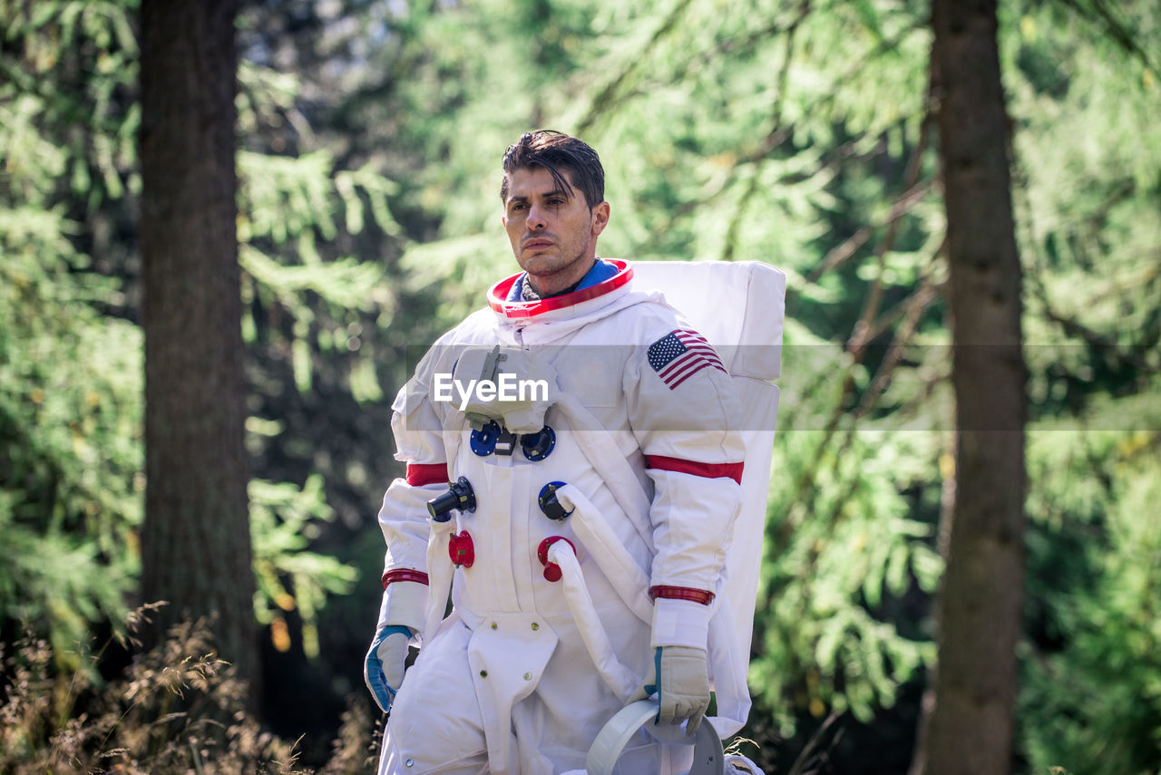 Astronaut looking away while standing in forest