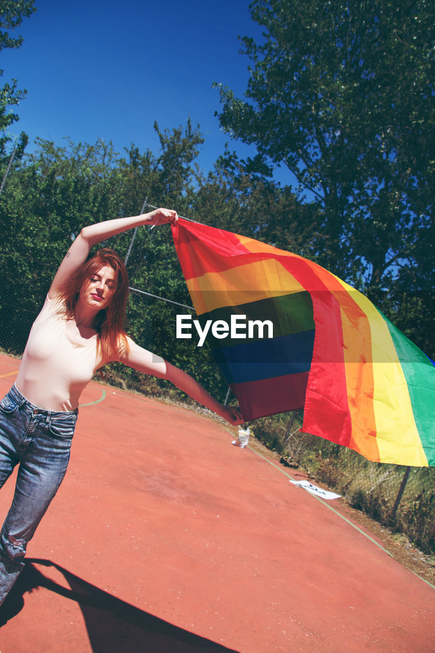 Portrait of young woman holding rainbow flag on sunny day