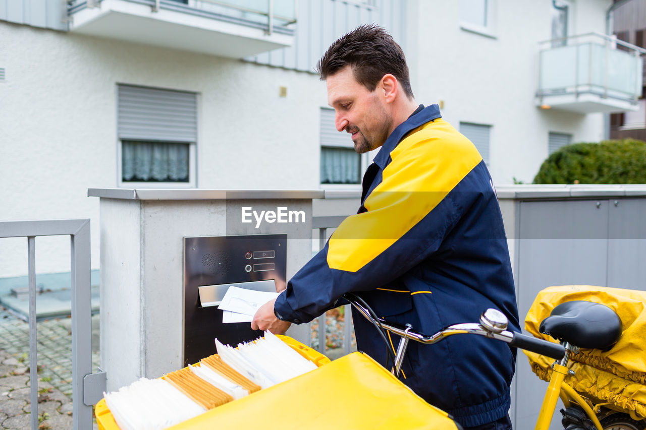 Side view of postal worker inserting letters in mailbox