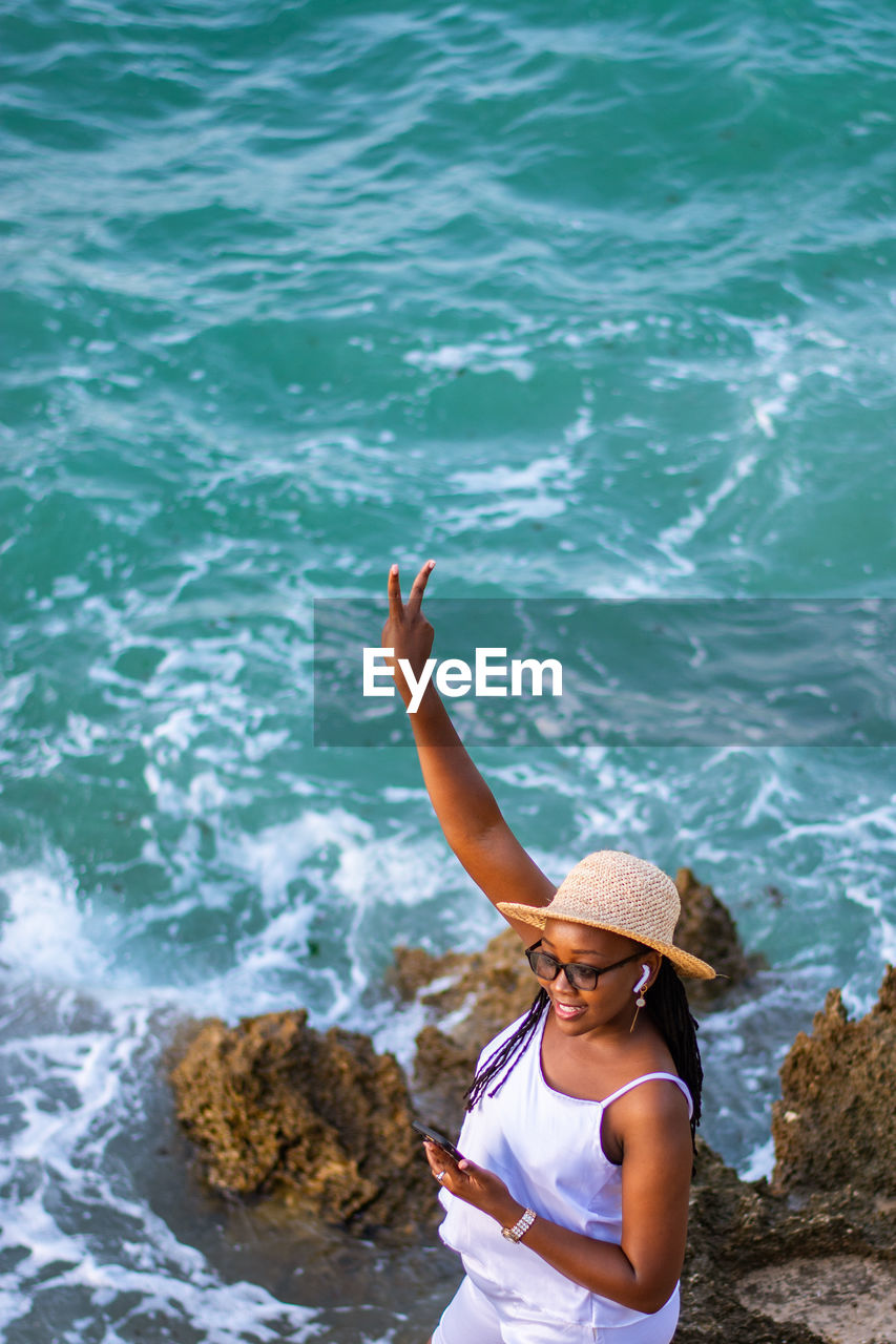 Scenic view of a young woman showing a peace sign at the beach 