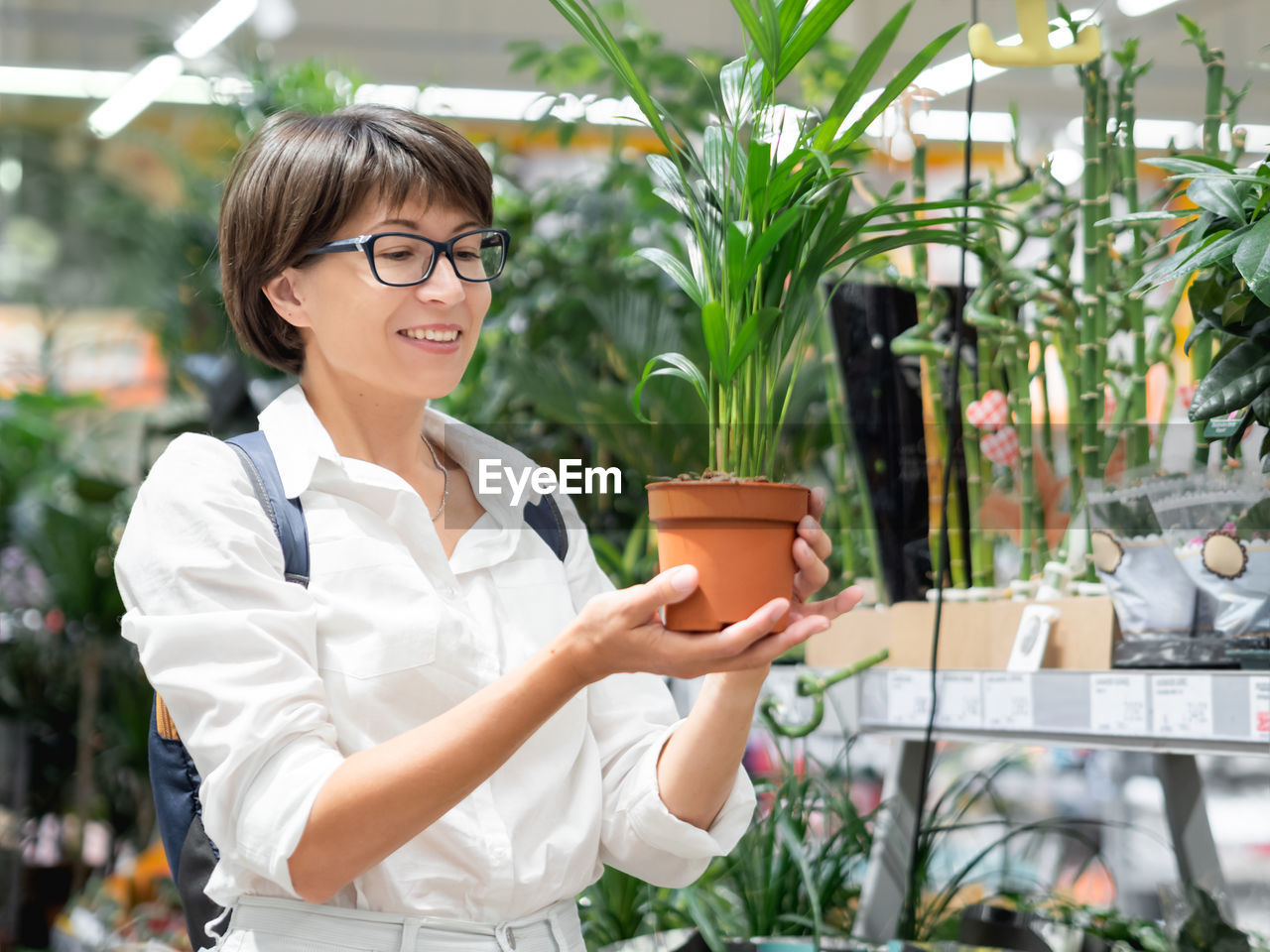 Woman chooses plants for home. shelves with seedlings, flowering plants and seeds in flower shop. 