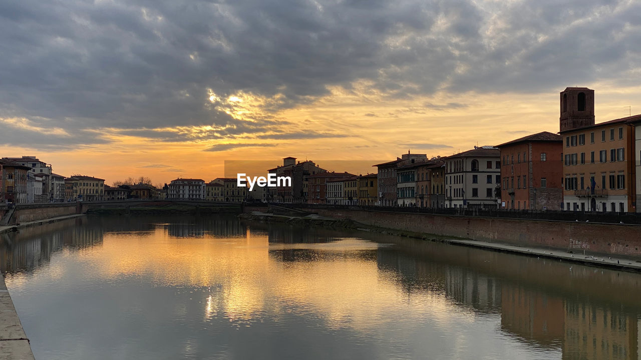 River by buildings against sky during sunset