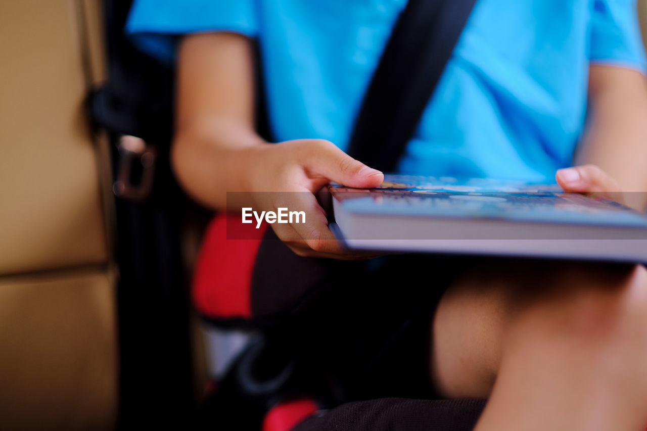 Midsection of boy holding book while sitting in car