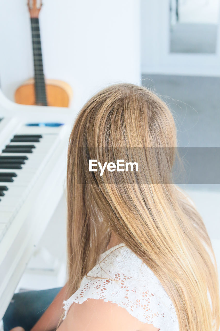 High angle view of blond woman sitting by grand piano at home