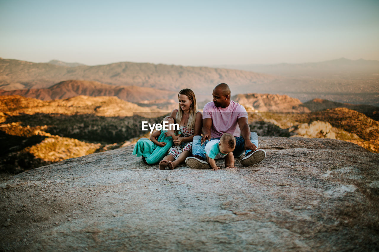 Family of four sitting on a large rock over looking desert city