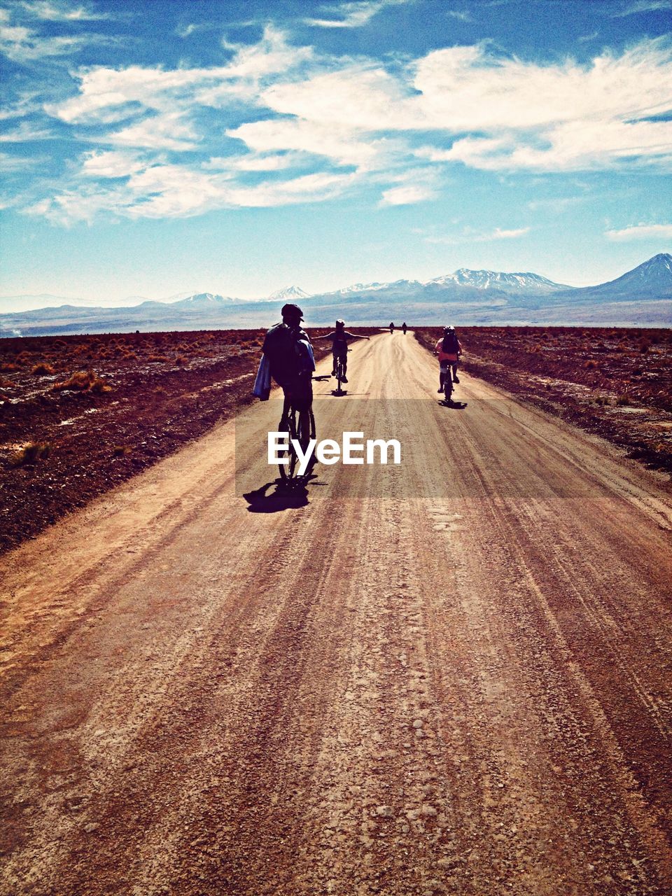 Rear view of people riding bicycle on dirt road