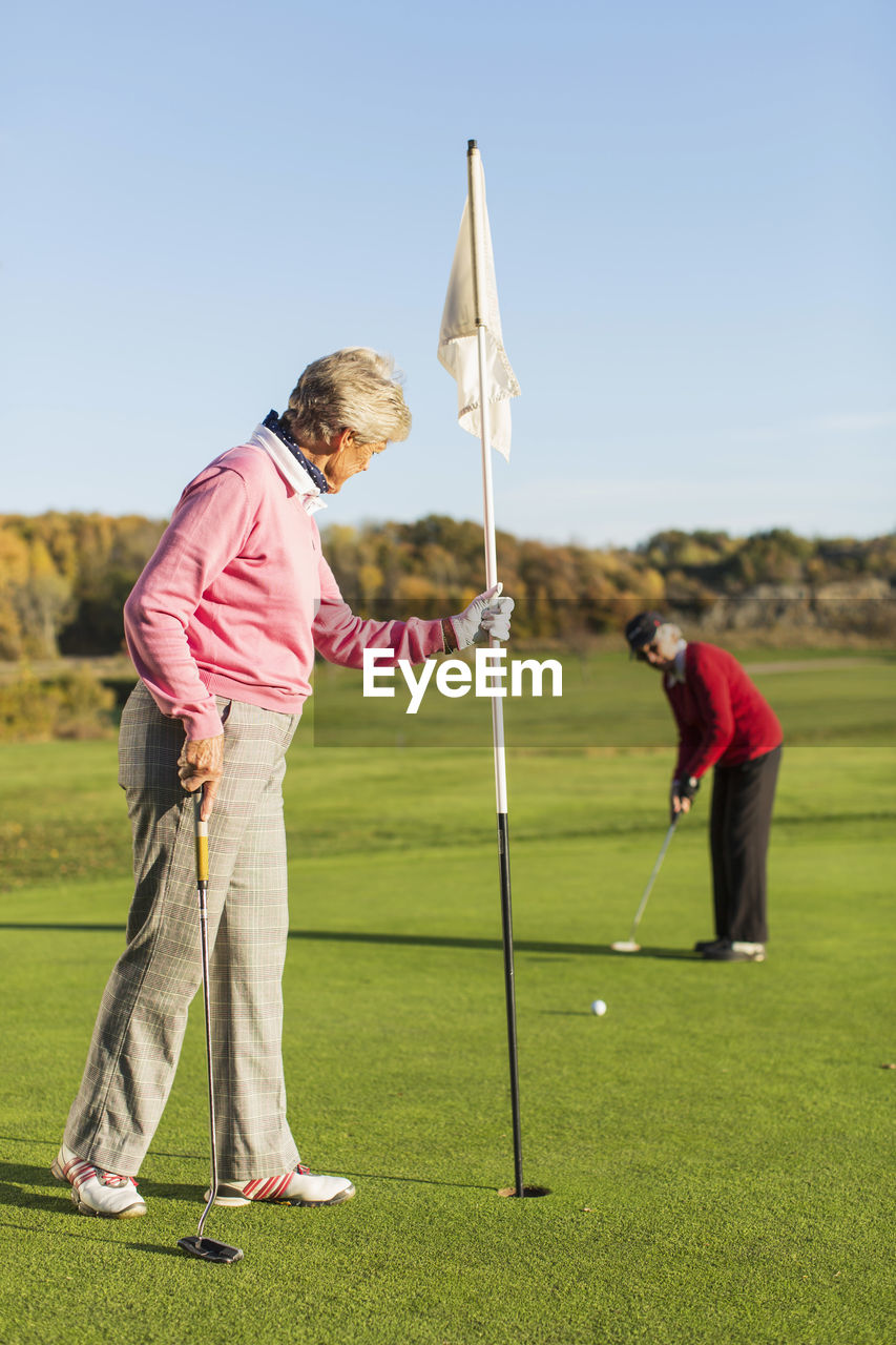 Senior woman putting while friend holding flag on golf course