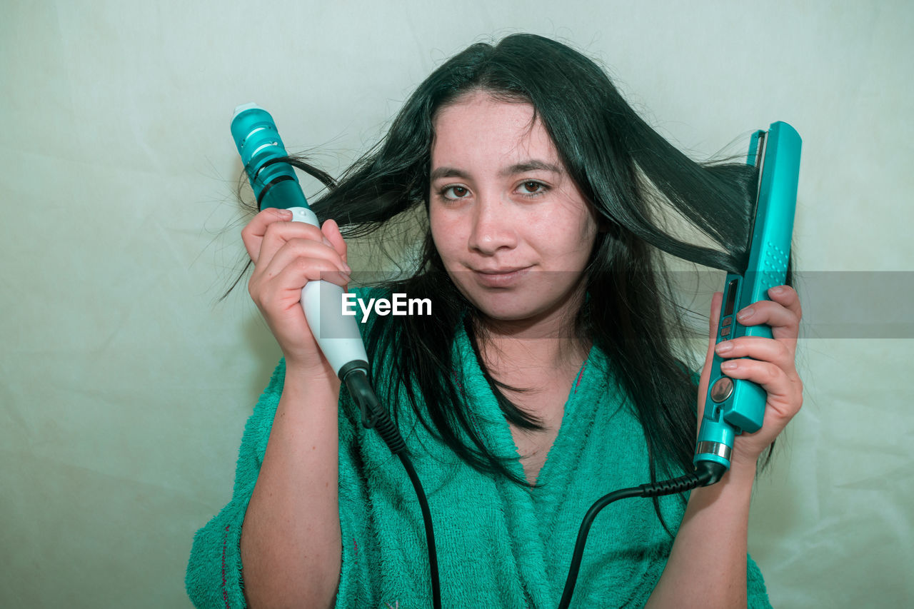 Close-up portrait of young woman holding curling tongs and hair straightener