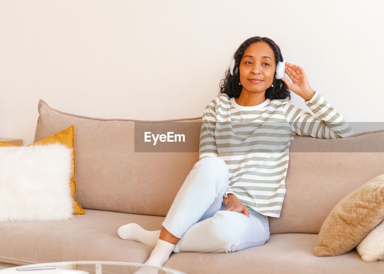 Smiling african-american female listening to music in headphones while sitting on couch