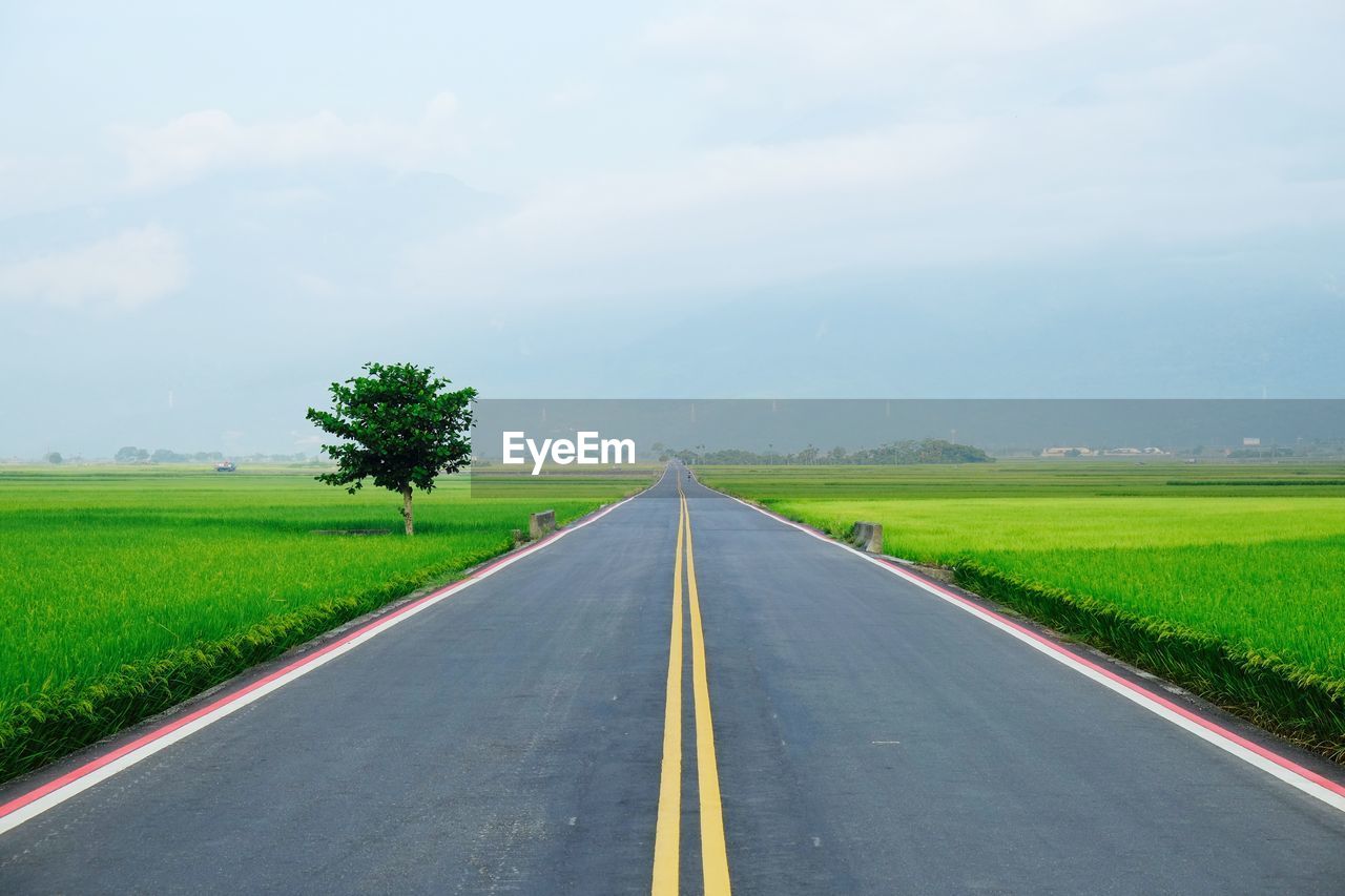 Empty road amidst grassy field against cloudy sky