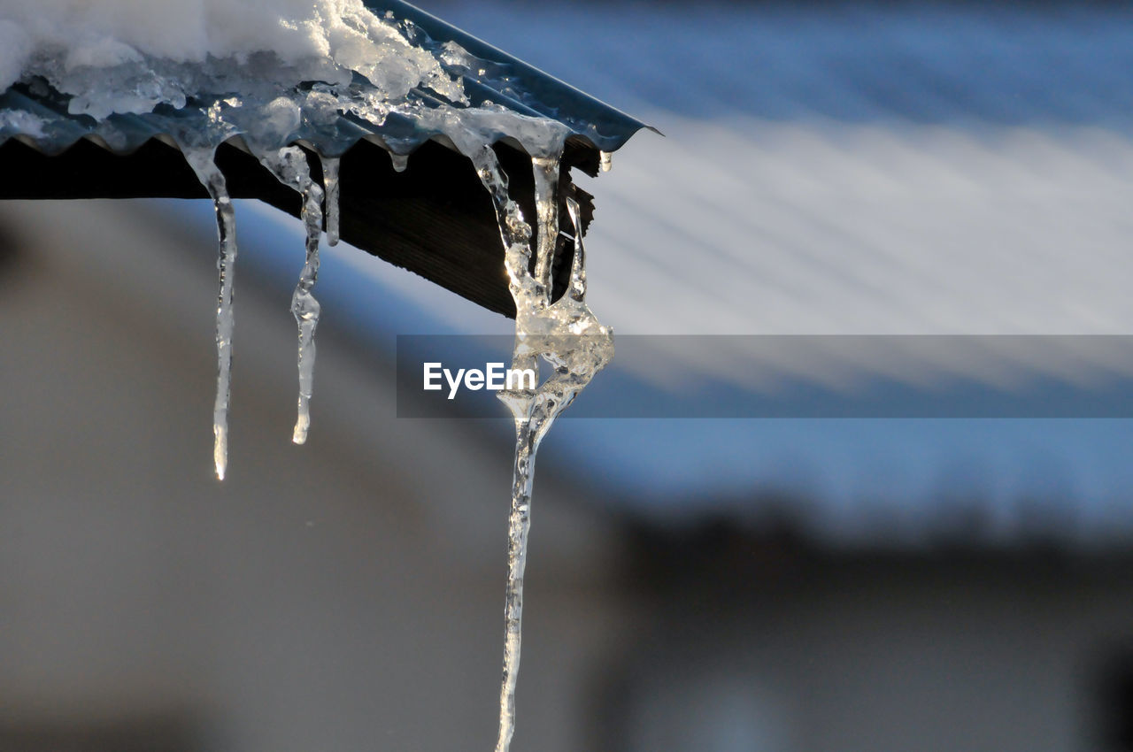 CLOSE-UP OF ICICLES ON ROOF AGAINST SNOW COVERED LANDSCAPE