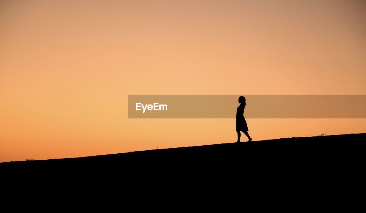 Silhouette woman walking on landscape against sunset sky