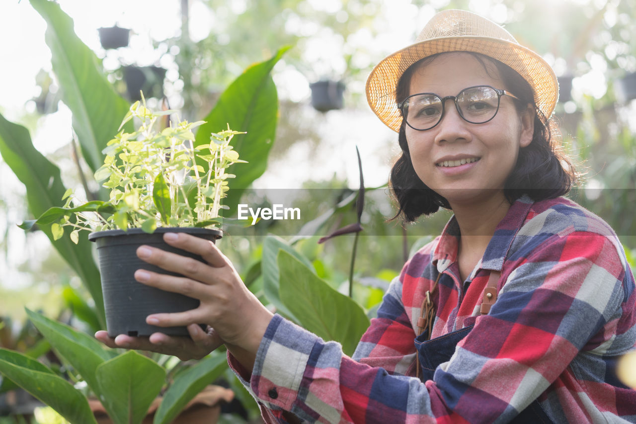 Portrait of smiling woman wearing hat holding potted plant