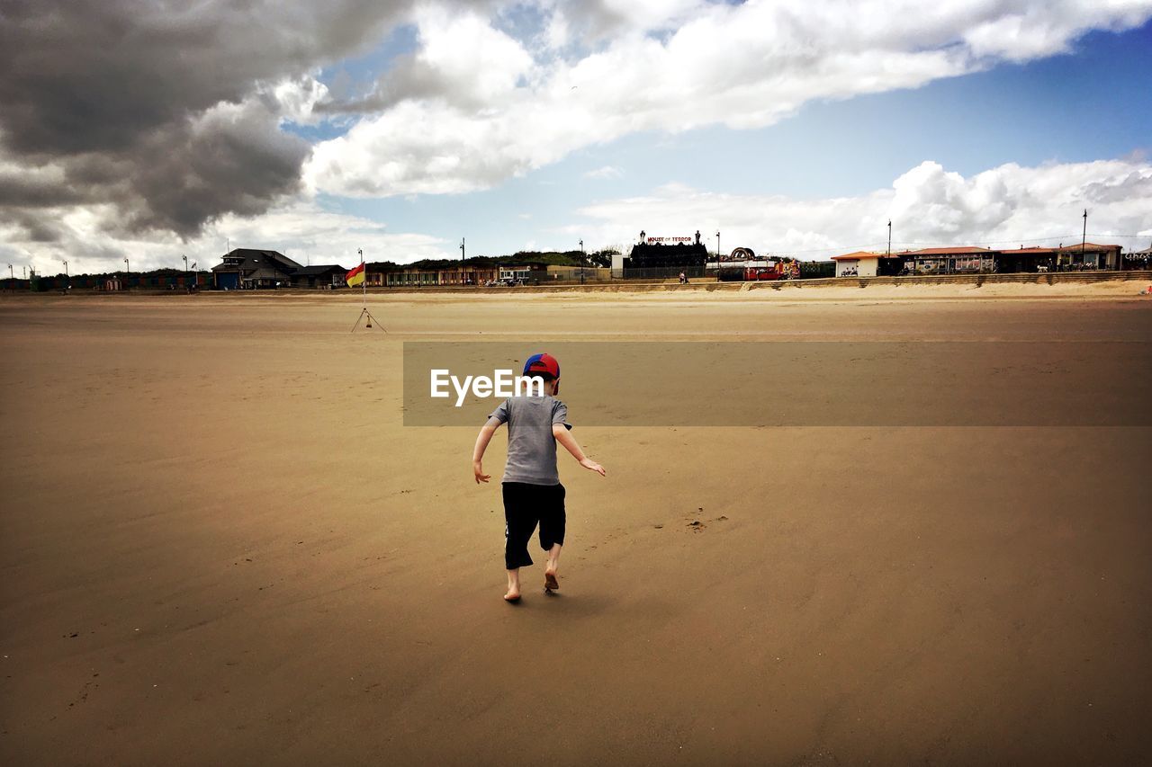 FULL LENGTH REAR VIEW OF BOY STANDING ON BEACH