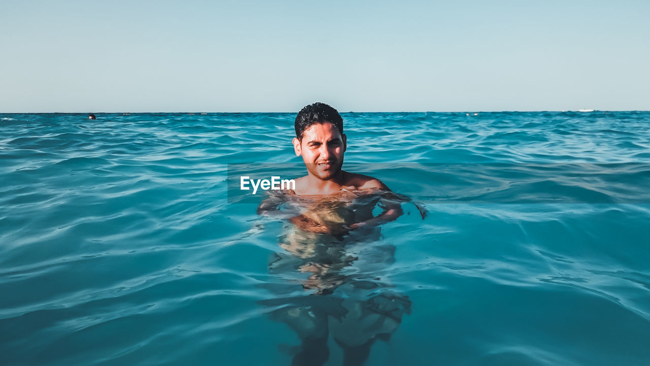 Portrait of shirtless man in sea against sky