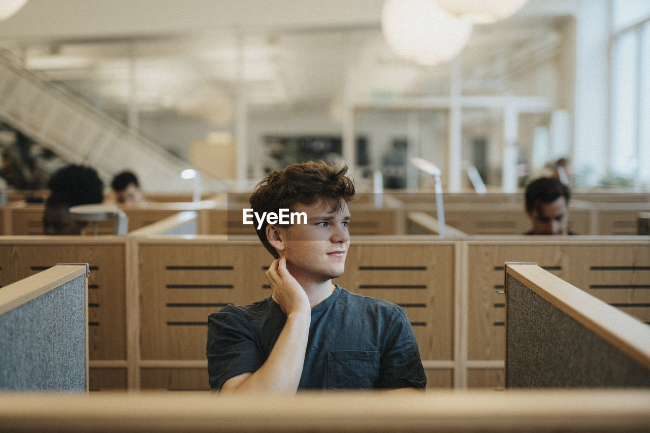 Smiling male student looking away while sitting in library at university