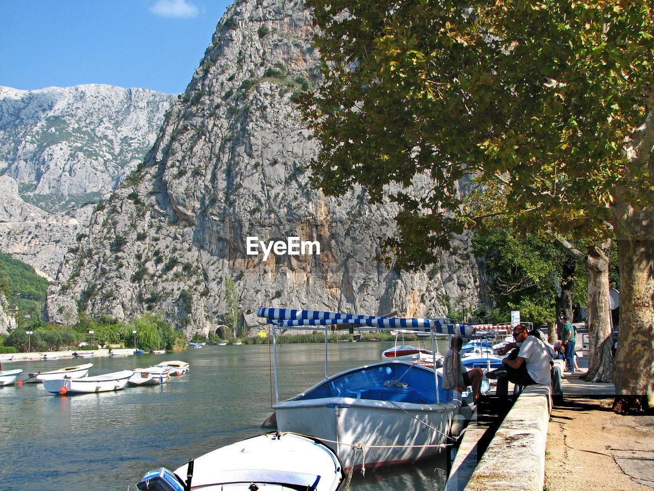 BOATS MOORED ON LAKE BY TREES AGAINST MOUNTAIN