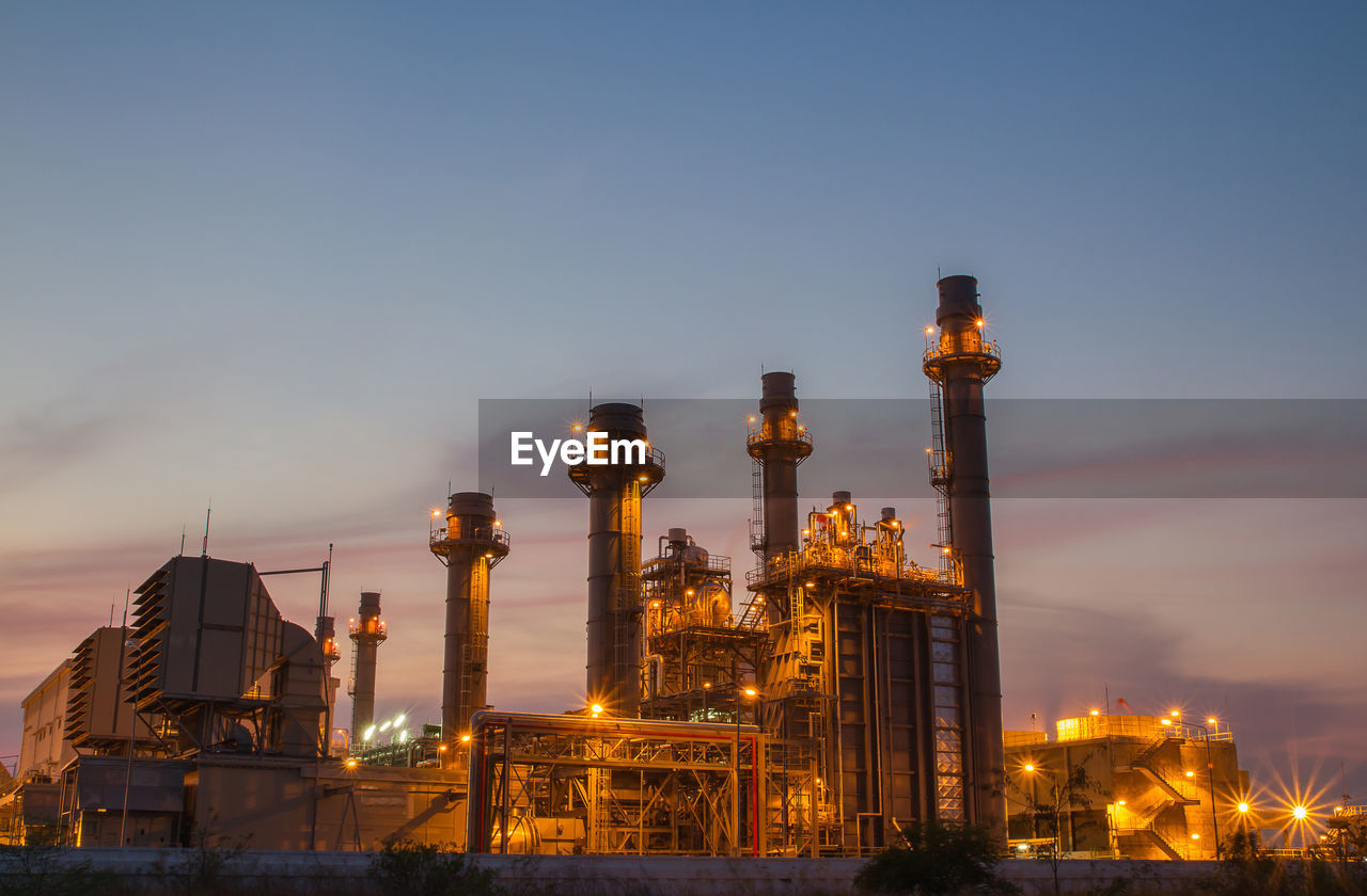 LOW ANGLE VIEW OF ILLUMINATED FACTORY AGAINST SKY