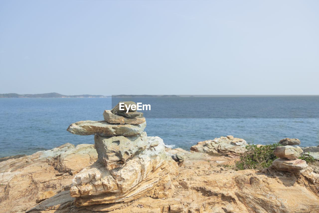 ROCKS ON SHORE AGAINST CLEAR SKY