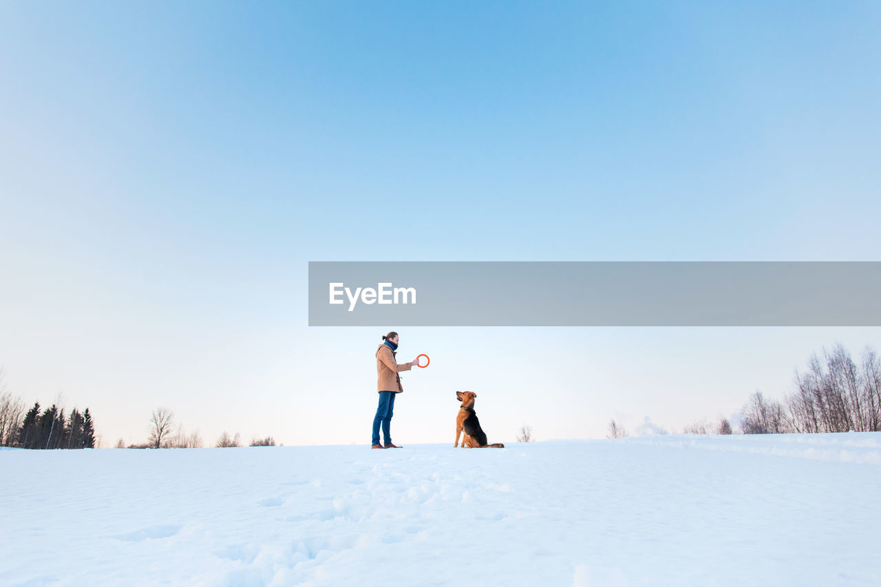 PEOPLE STANDING ON SNOW FIELD AGAINST CLEAR SKY