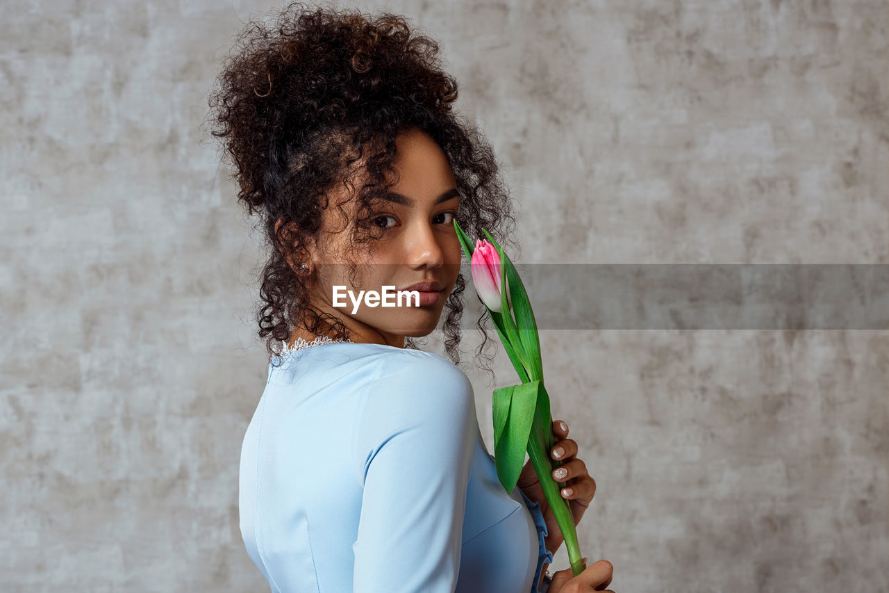 Portrait of smiling young woman holding tulip while standing against wall