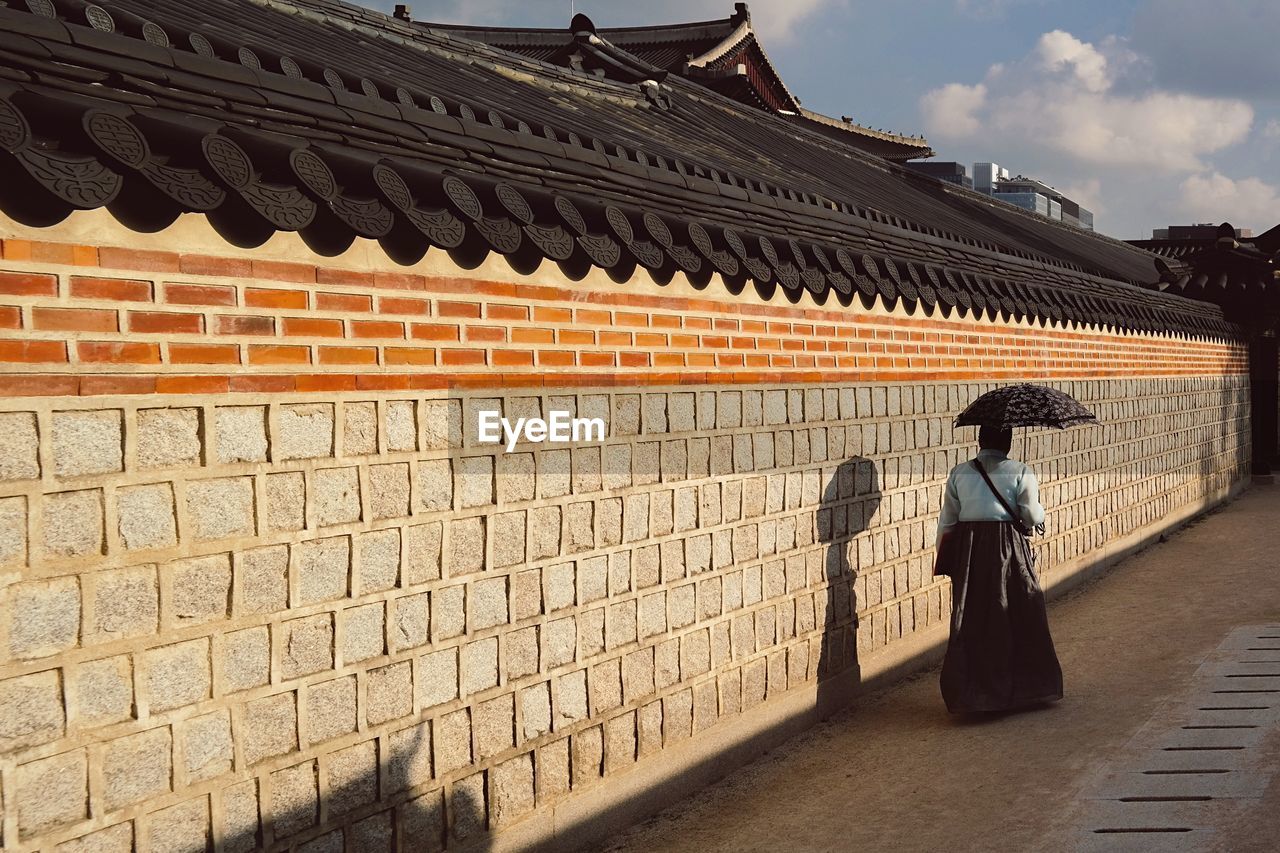 Rear view of woman walking while holding umbrella with shadow on wall