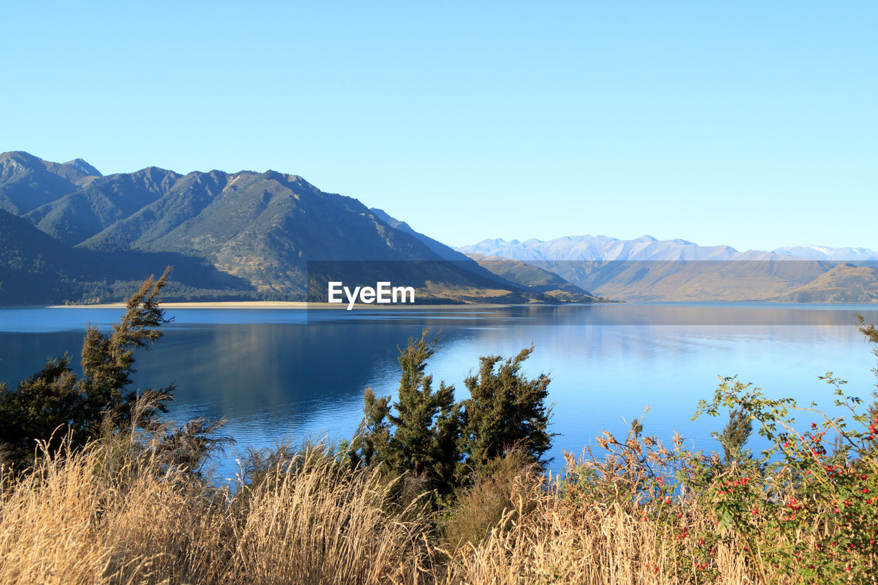 Scenic view of lake and mountains against clear blue sky