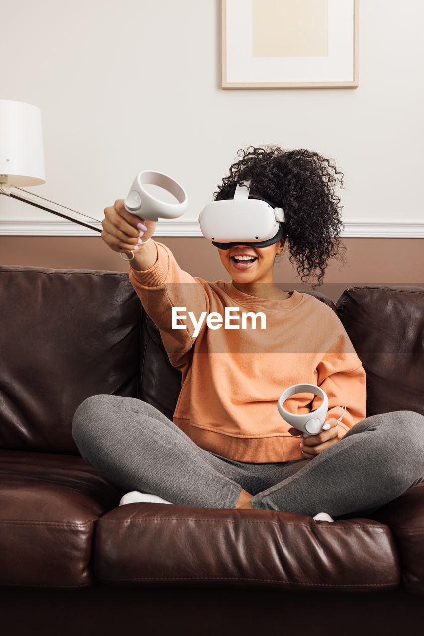 Young woman wearing virtual reality simulator while sitting on sofa at home