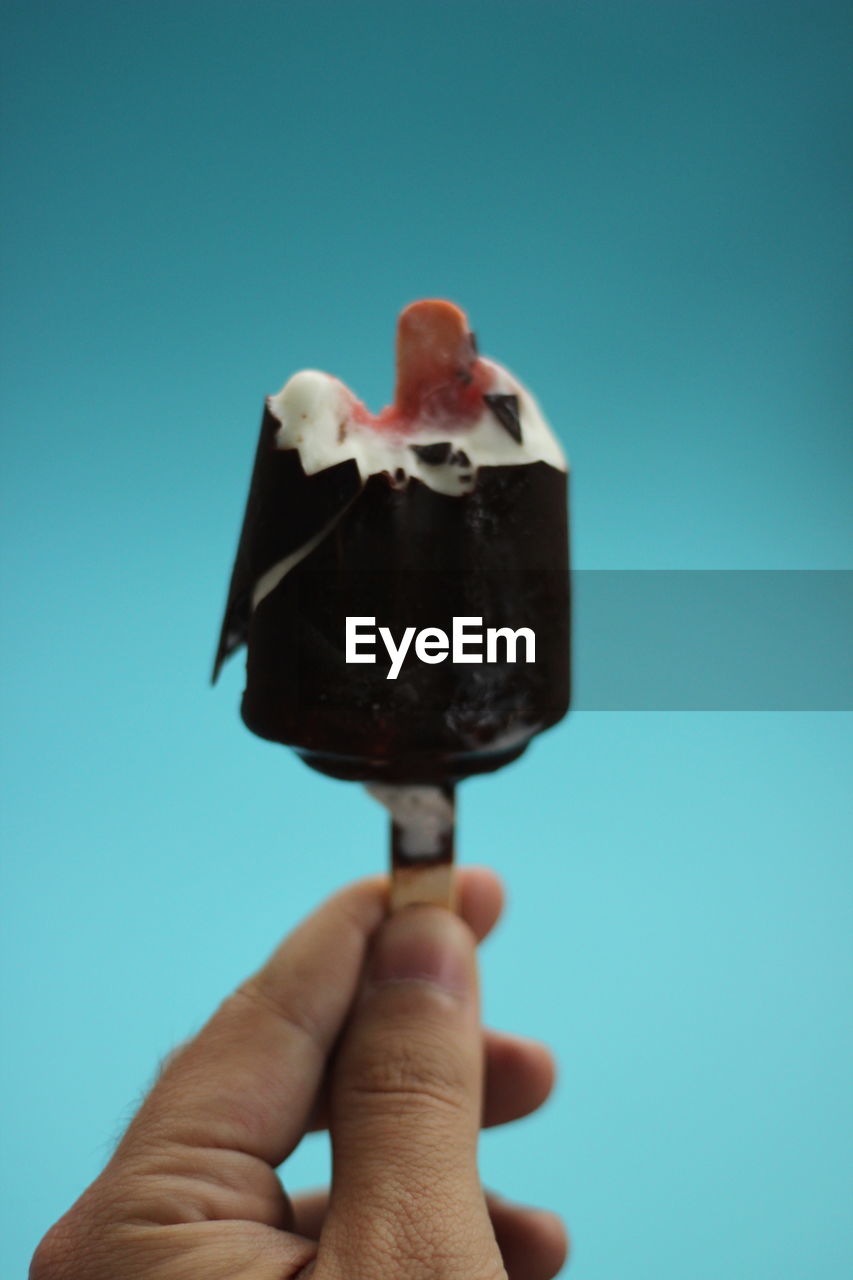 HUMAN HAND HOLDING ICE CREAM AGAINST BLUE SKY