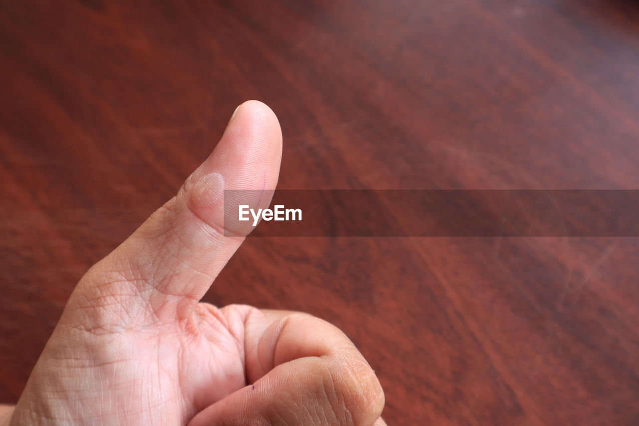Close-up of cropped hand showing thumbs up sign on table