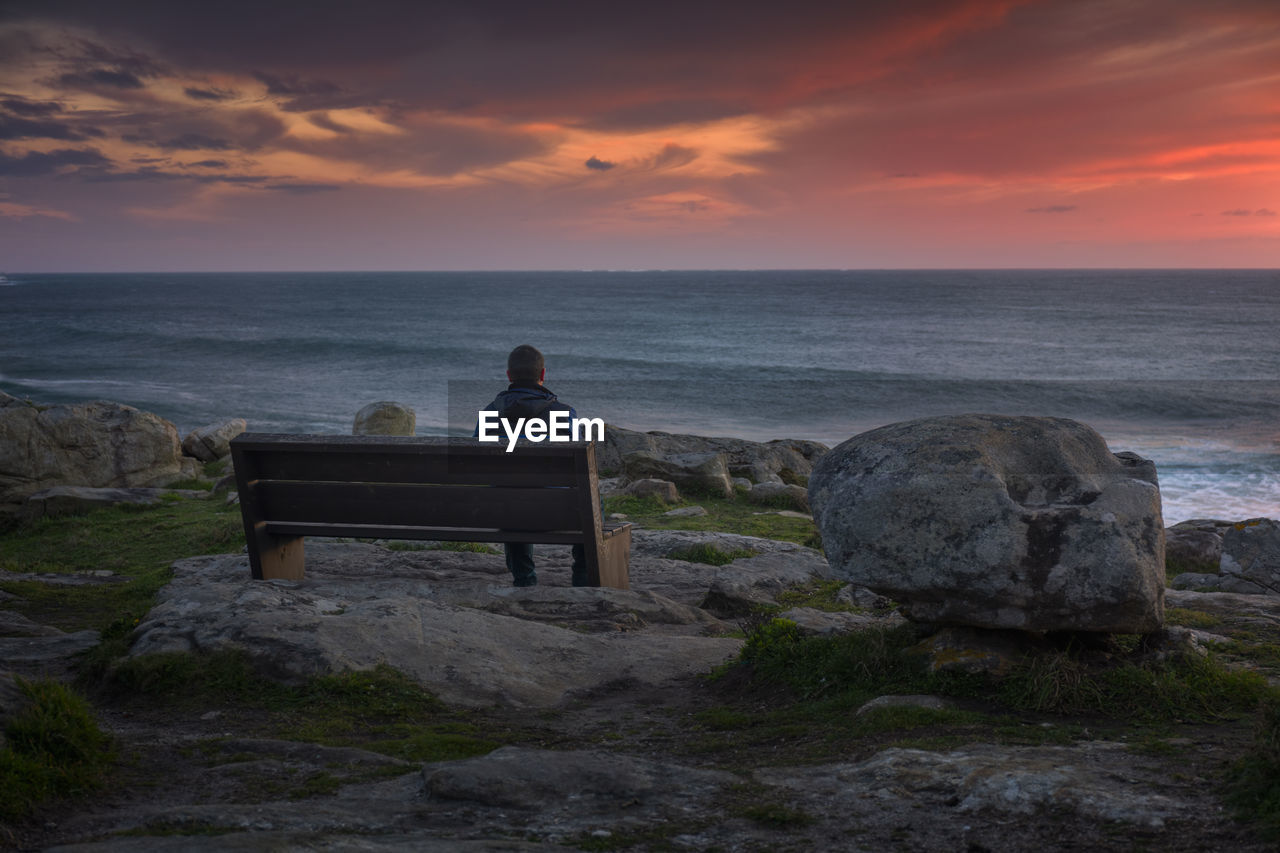 Man watching a stunning sunset sitting on a bench on the coast