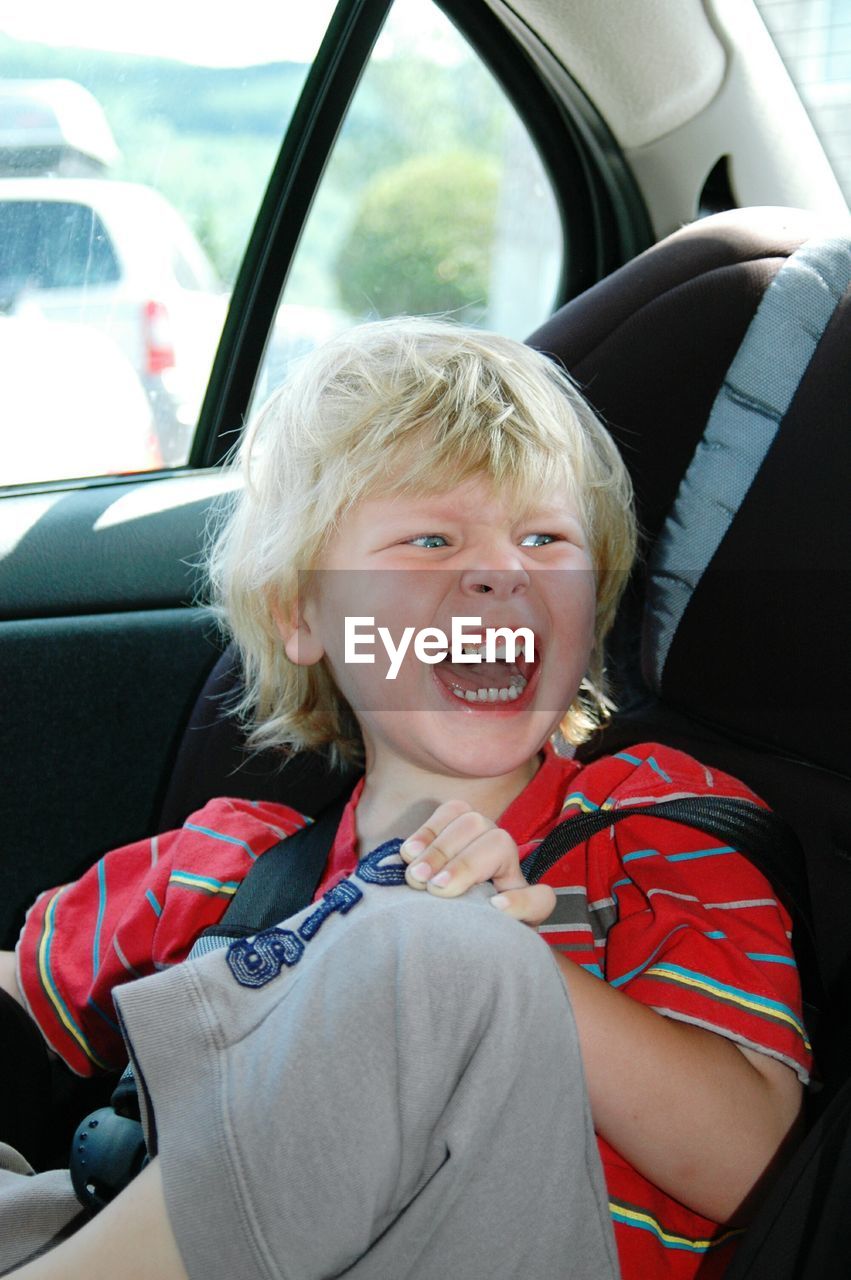 Cute cheerful boy looking away while sitting in car