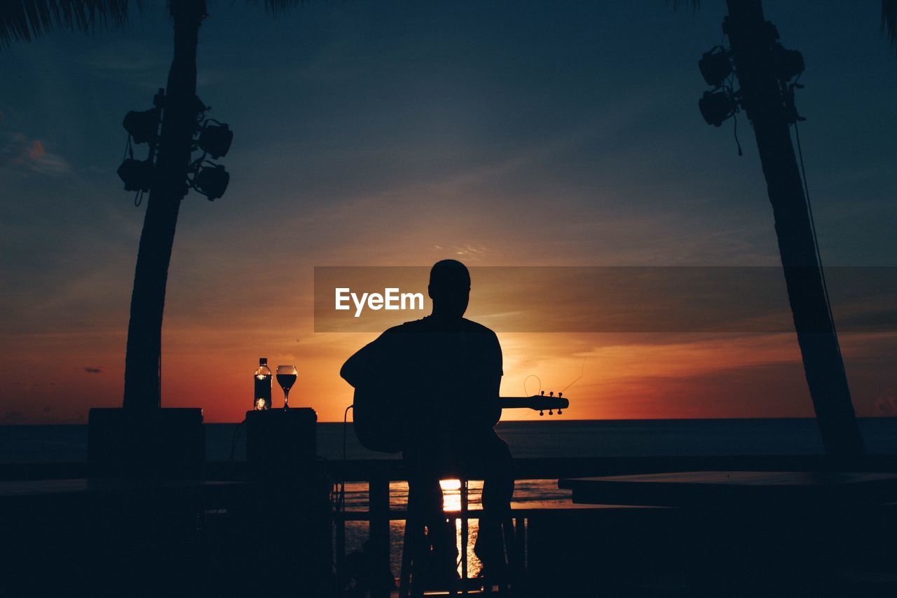 Silhouette man sitting by sea against sky during sunset