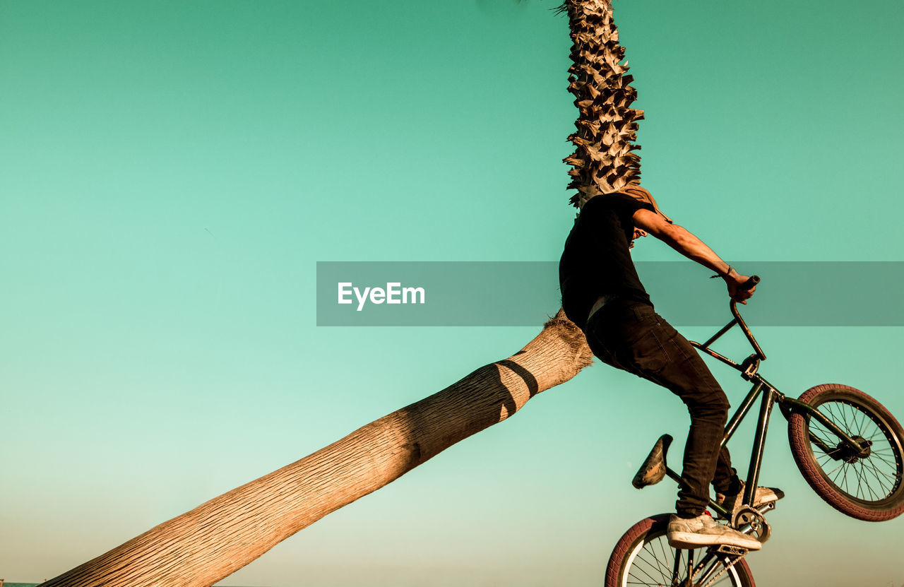 Low angle view of man with bicycle performing stunt against clear sky