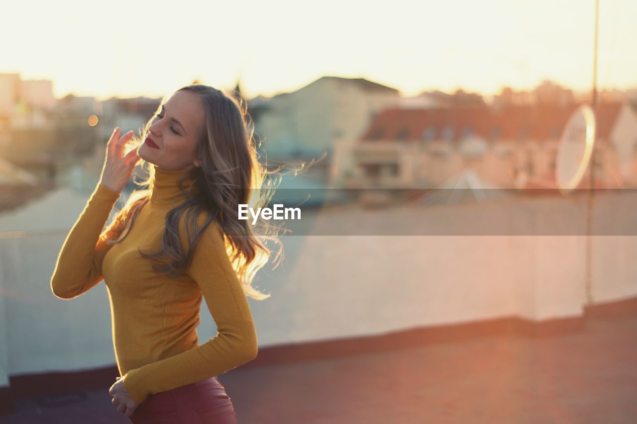 Woman standing against buildings in city during sunset