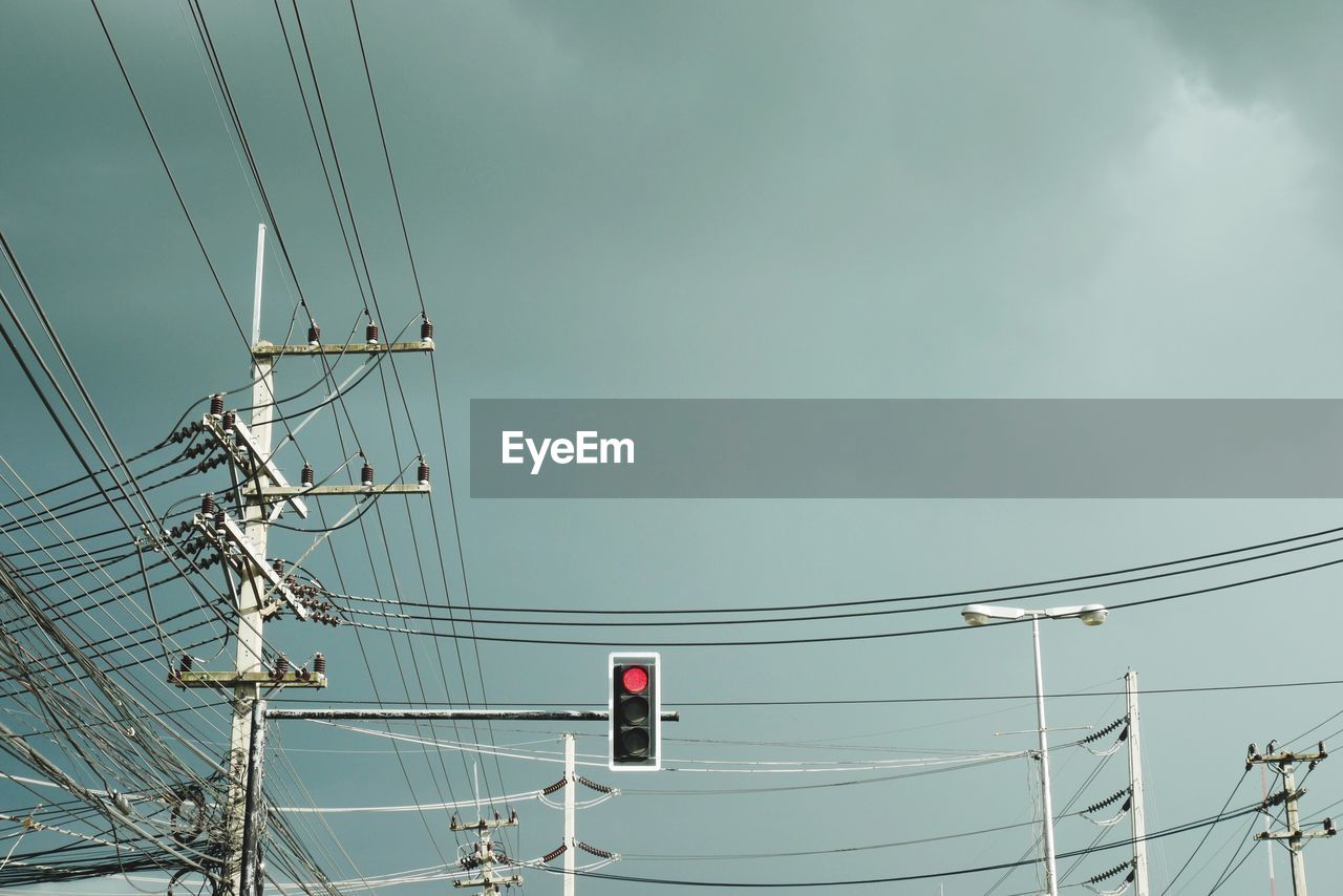 Low angle view of tangled cables by traffic signal against sky