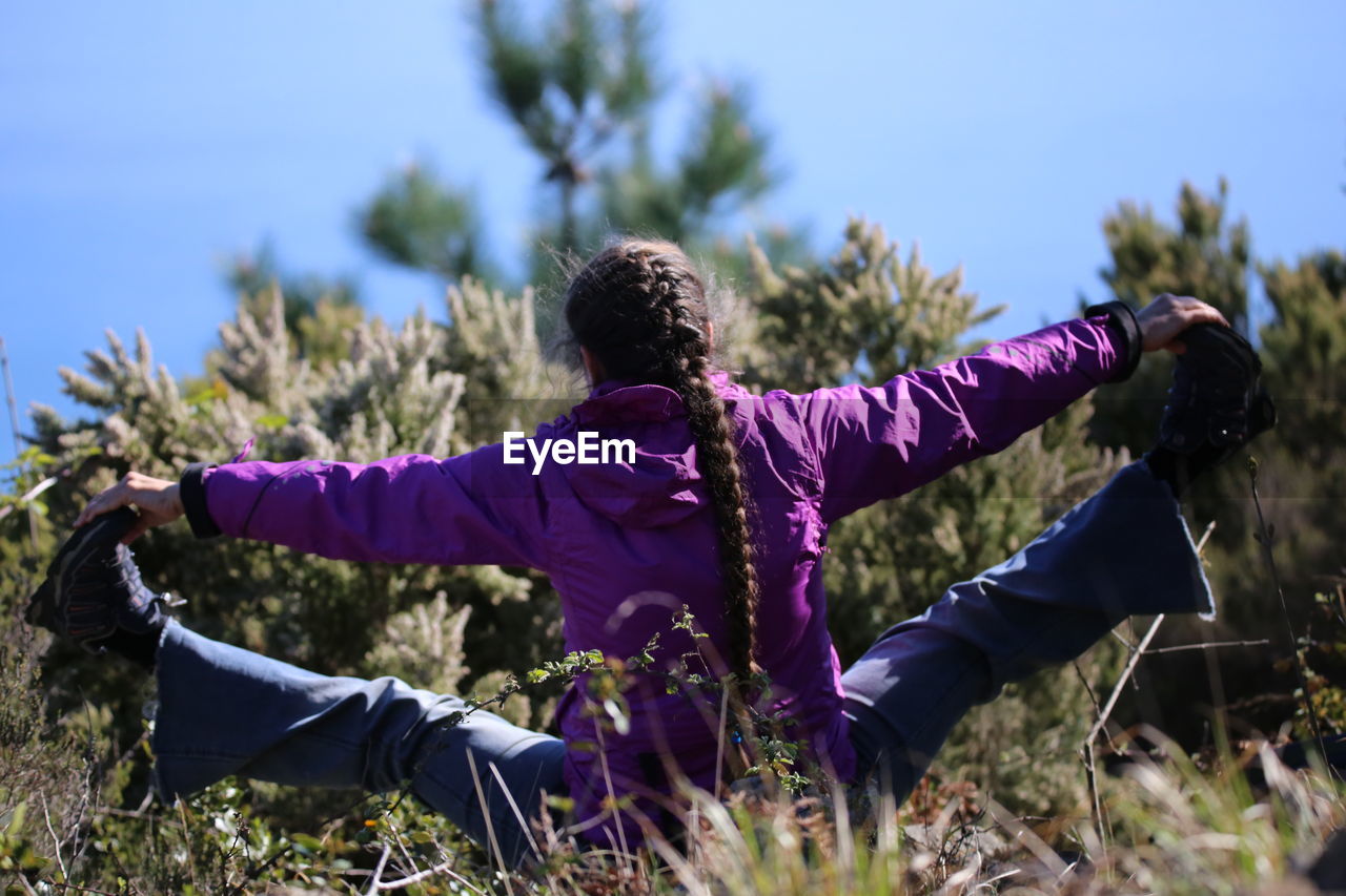 Rear view of woman stretching legs on field against trees