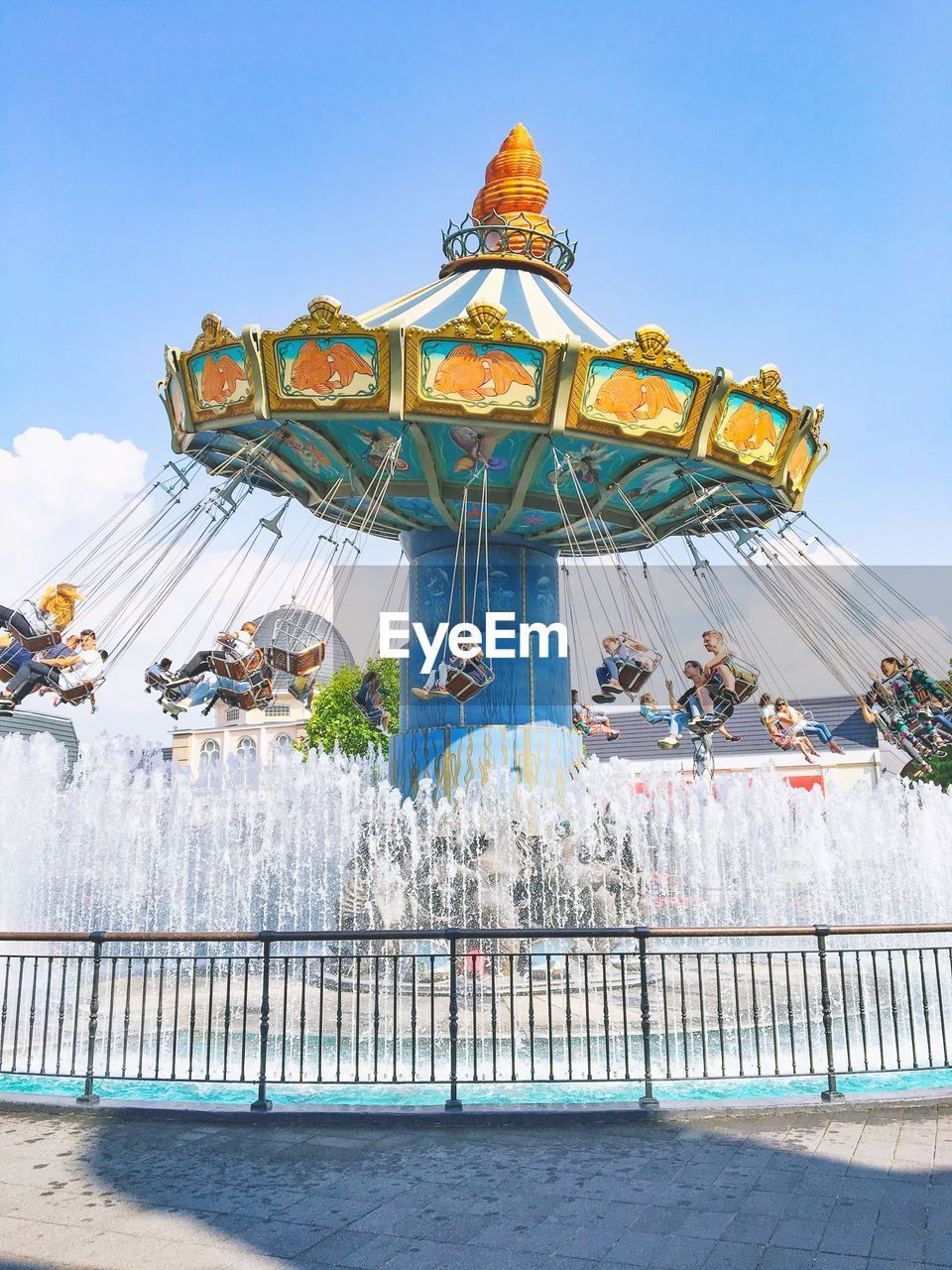 Chain swing ride over fountain against blue sky at amusement park