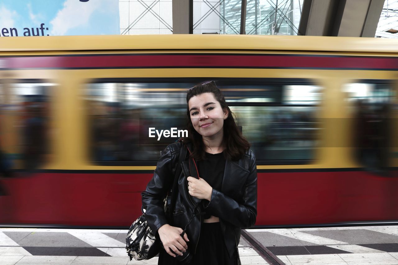 Portrait of smiling woman standing against moving train