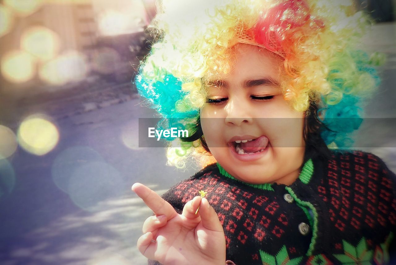 Playful boy wearing colorful wig sticking out tongue on road