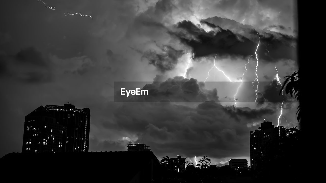 Low angle view of lightning over cityscape against dramatic sky