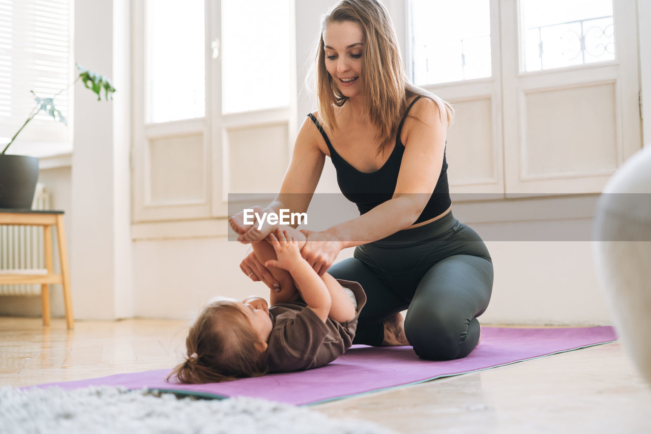 Young woman fit mom with baby girl doing fitness on mat at home