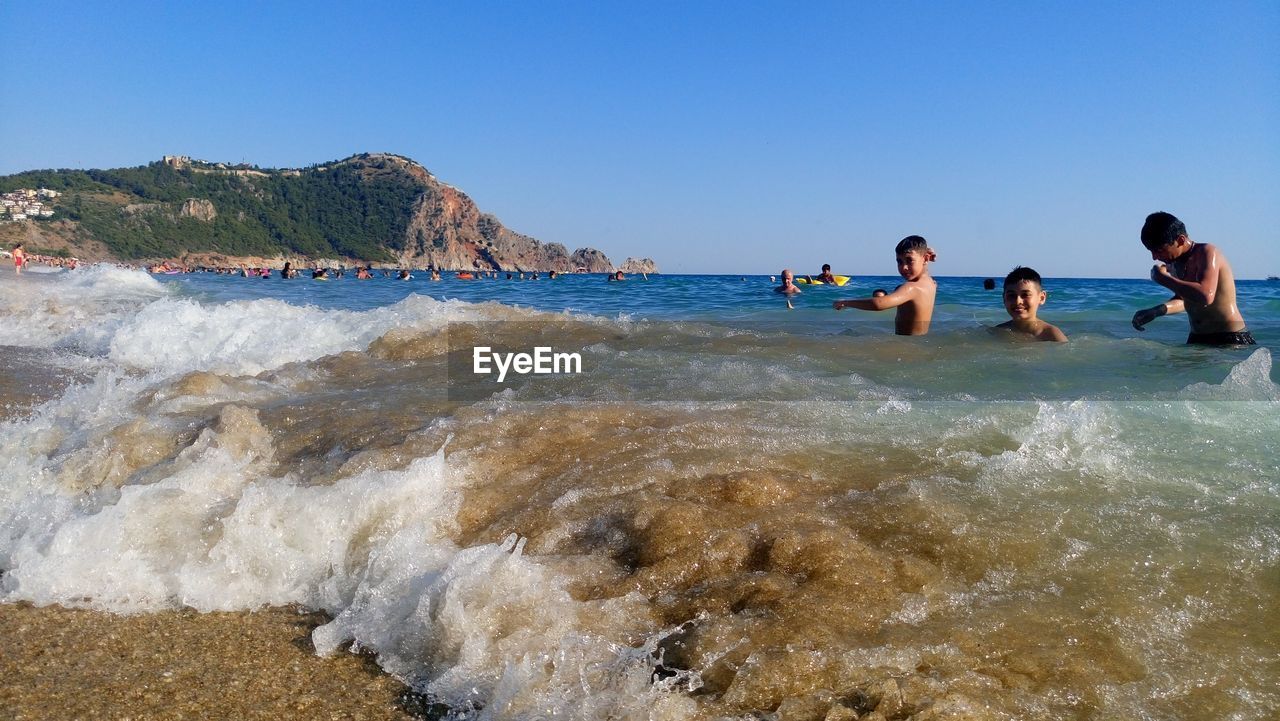 Boys swimming in sea against clear sky