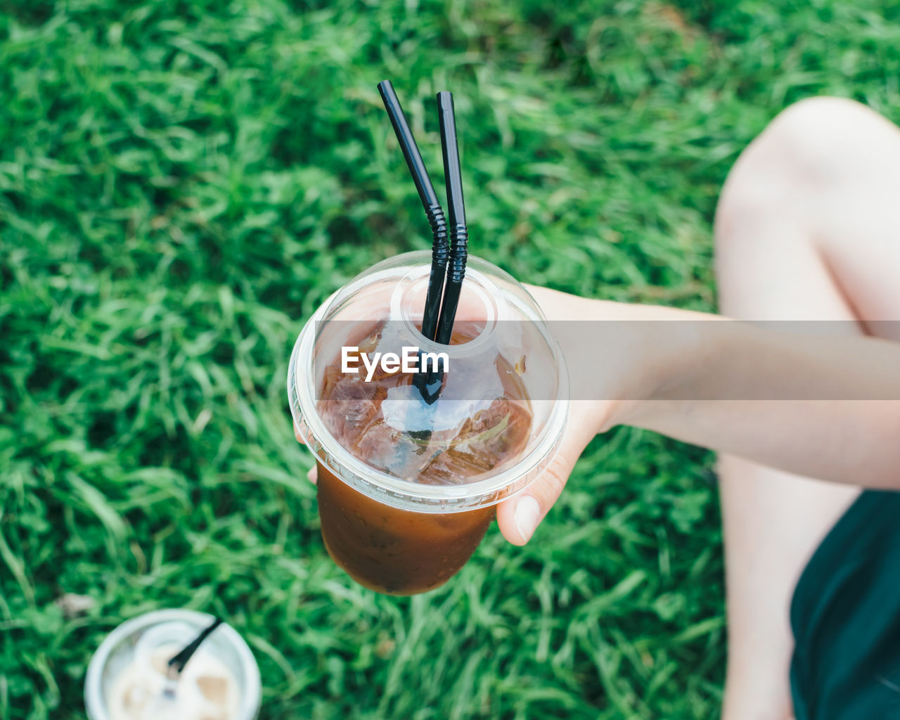 Cropped image of person holding latte at grassy field