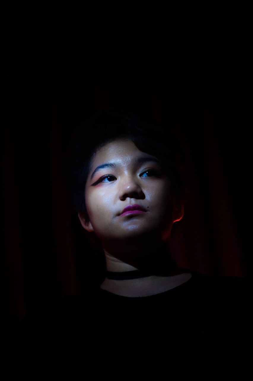 darkness, portrait, one person, black background, black, indoors, headshot, studio shot, young adult, front view, copy space, dark, looking, human face, women, adult, light, contemplation, looking at camera, looking up, serious, child, close-up, childhood, mystery