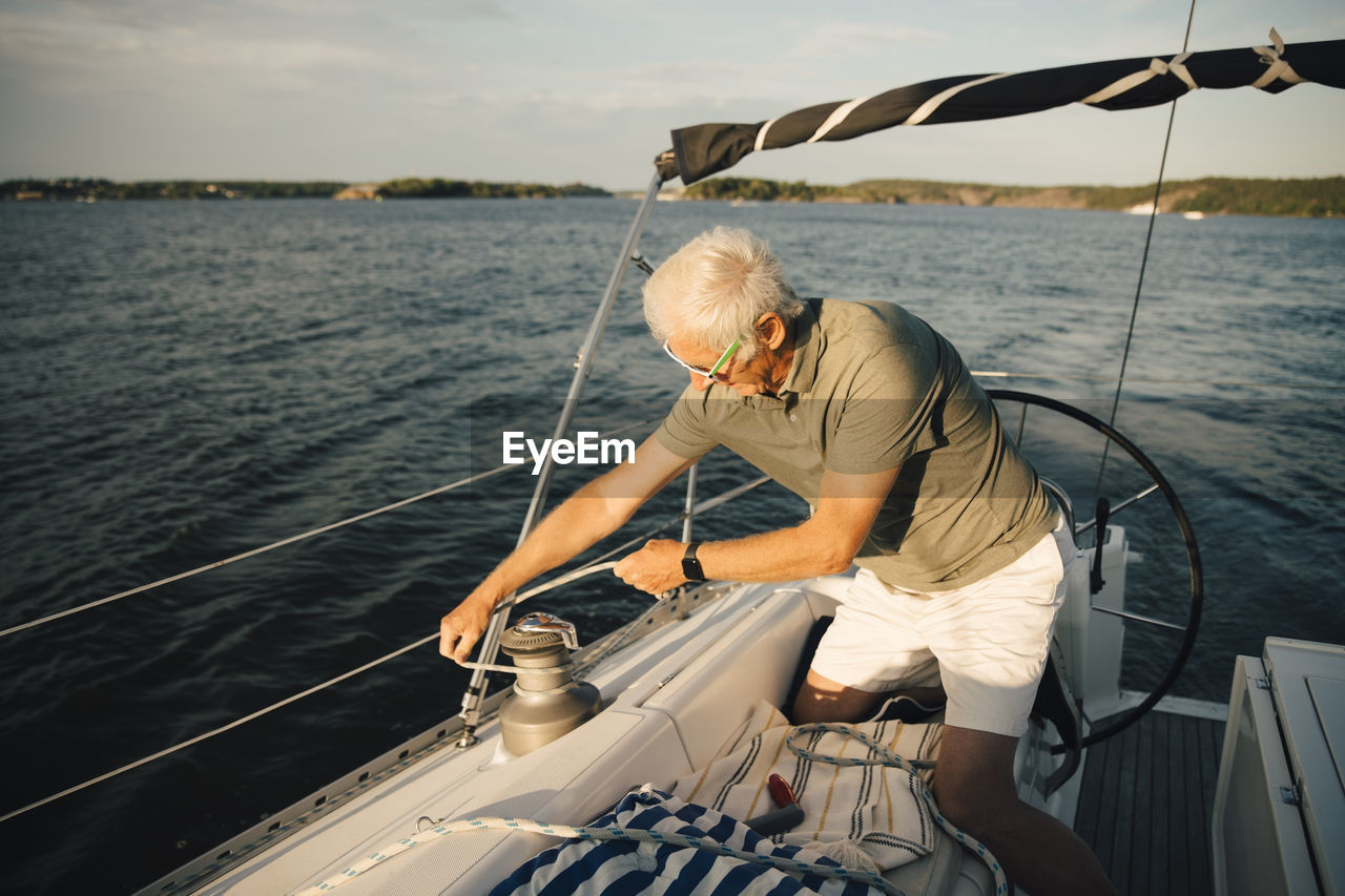 Senior man tying rope on cleat while kneeling in boat during sunny day